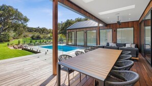 Eine moderne Außenterrasse mit Holztisch und -stühlen, einem Pool und einer gläsernen Lounge-Ecke.