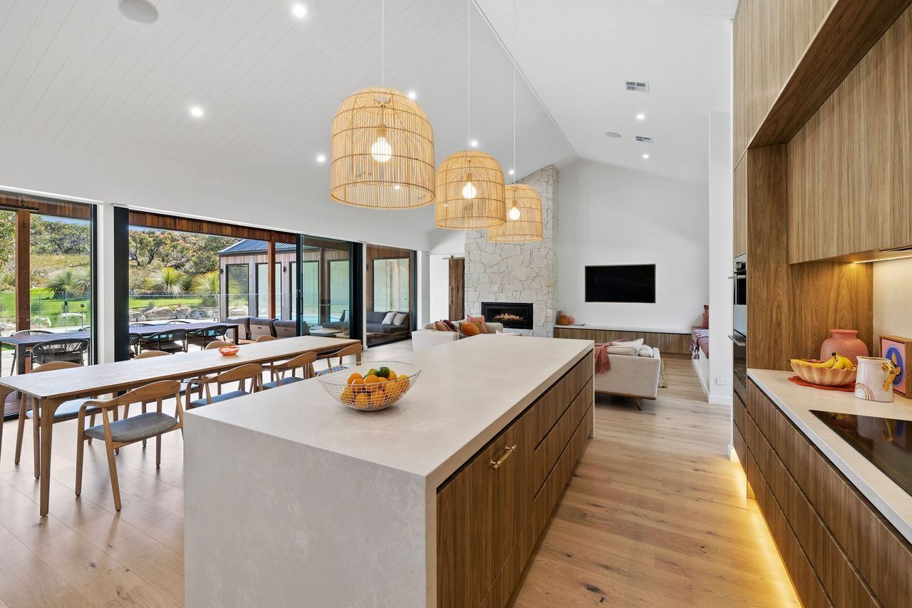 A modern kitchen with a large island, wooden cabinets, and pendant lighting.