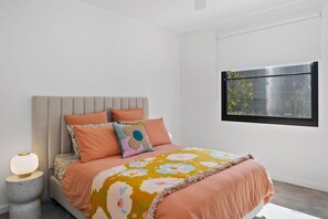Ein Schlafzimmer mit einem Bett, Kissen, einer Nachttischlampe und einem Fenster mit Blick auf Grünflächen.