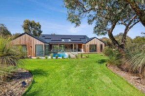 A modern house with a swimming pool, large windows, and a well-maintained lawn.