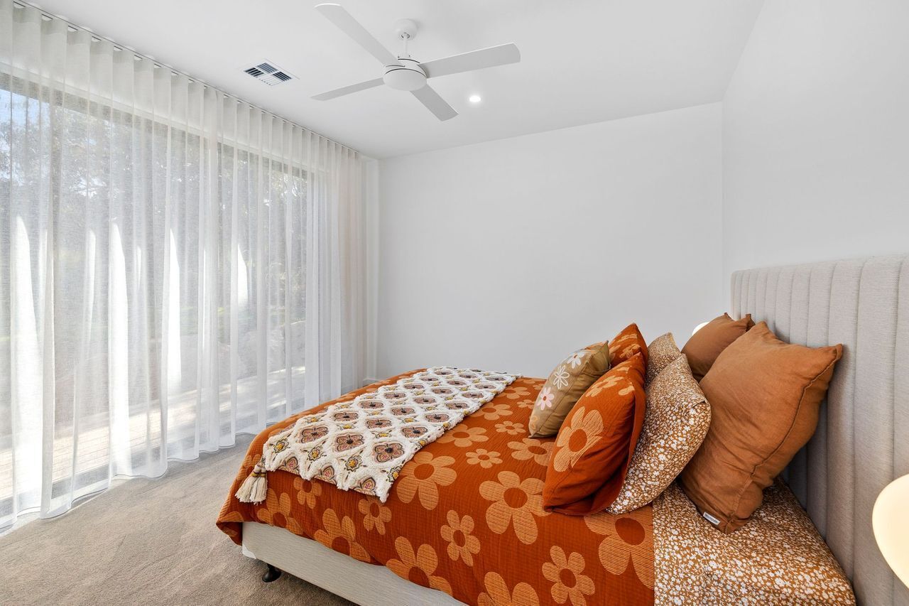 A bedroom with a bed, a ceiling fan, and sheer curtains.