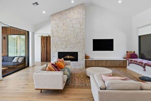 Una sala de estar moderna con chimenea de piedra, televisor de pantalla plana y un ventanal grande.