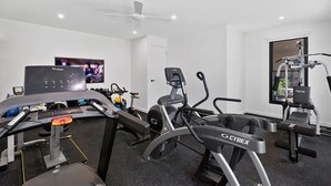 Ein Fitnessraum mit Cardiogeräten, einem Fernseher und einem Deckenventilator.