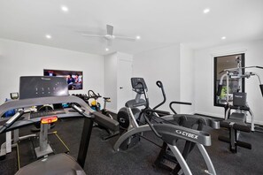 Un gimnasio con máquinas de cardio, un televisor y un ventilador de techo.