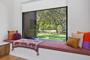 A room with a large window, a bench with cushions, and a view of a garden.