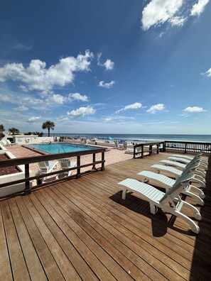 A wooden deck with lounge chairs, a swimming pool, and a view of the ocean. - Oceanfront paradise! Book now and save! (Daytona Beach)