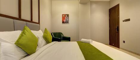 A hotel room with a large bed, green pillows, a green throw, a chair, and a door.