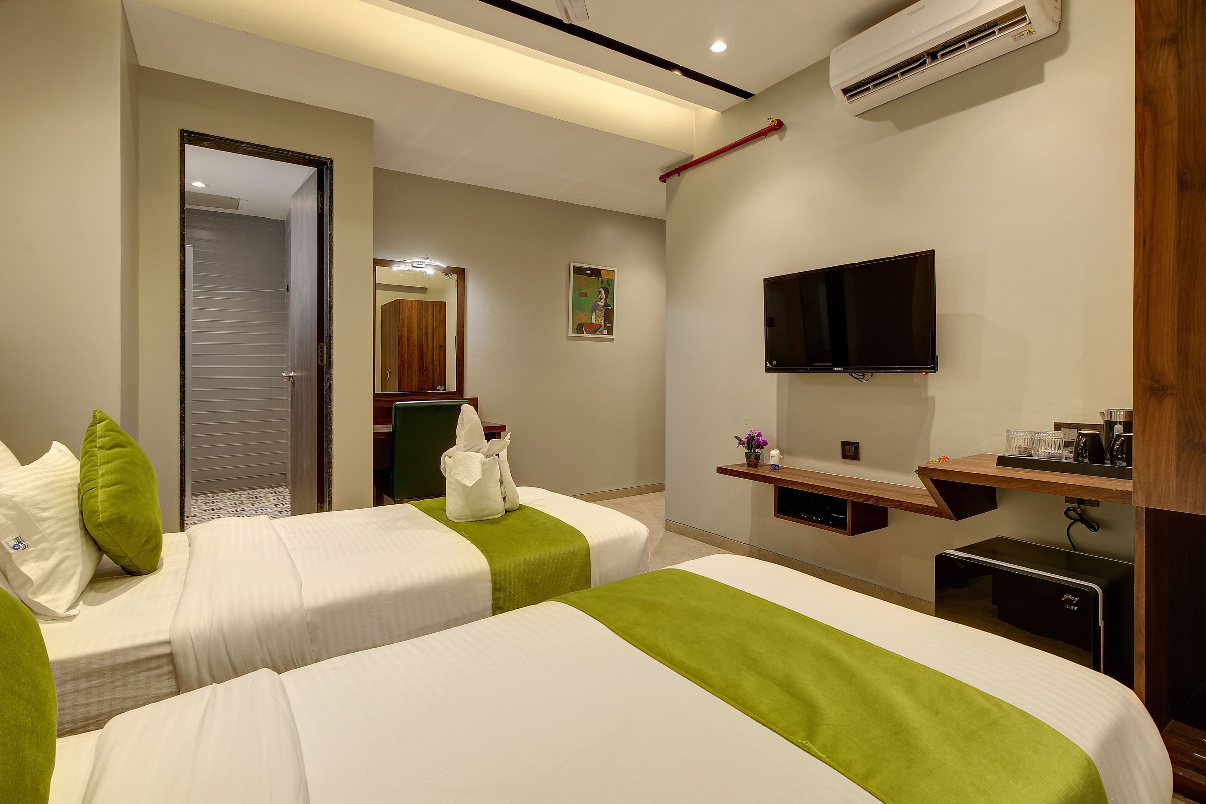 Habitació d'hotel amb dos llits, televisió, escriptori petit i aire condicionat.