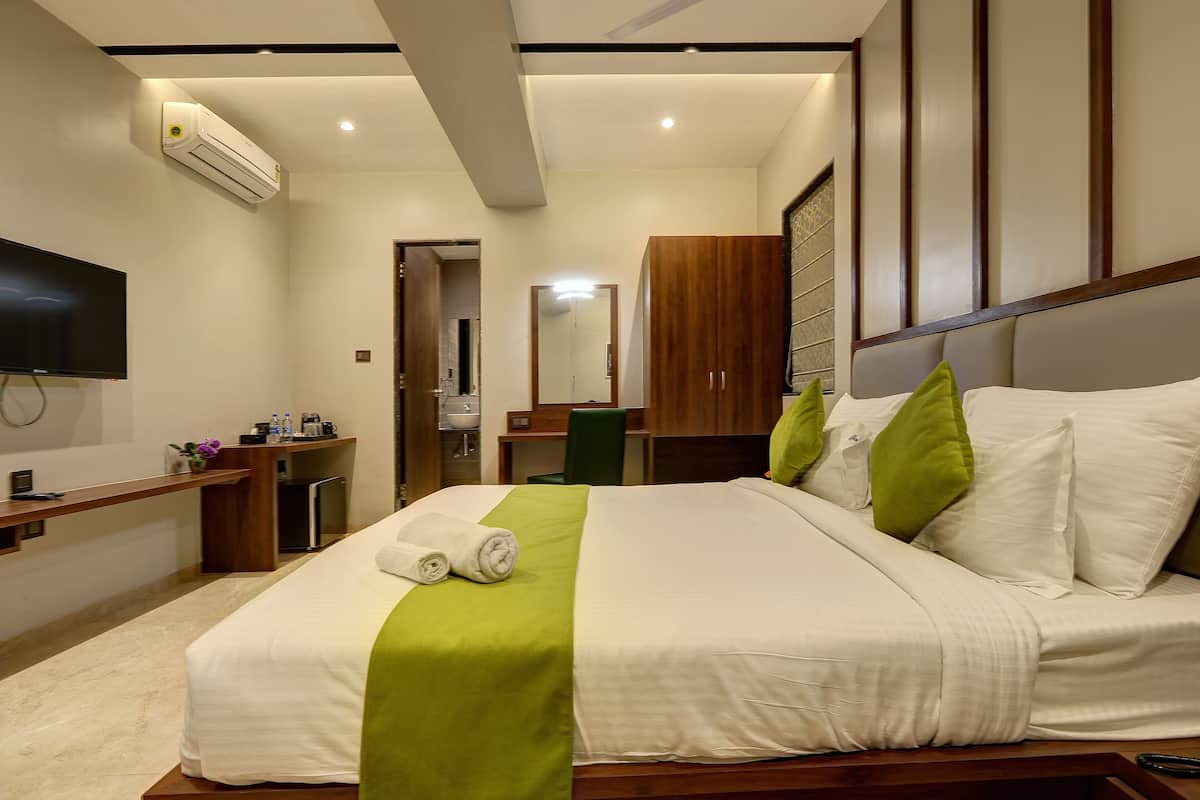 A hotel room with a bed, a desk, a TV, and an air conditioning unit.