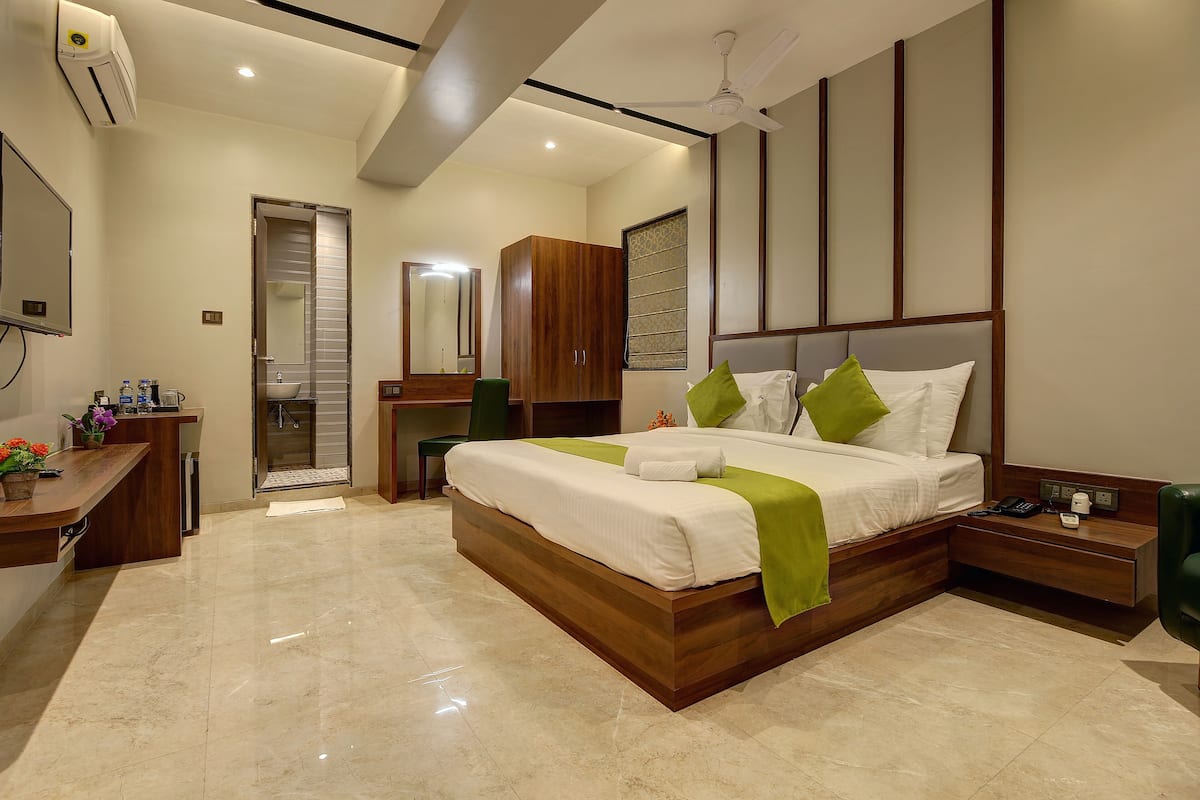 A modern hotel room with a large bed, a desk, a wardrobe, and a bathroom.