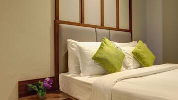 A neatly made bed with white linens and two green pillows, a wooden nightstand with a vase of purple flowers, and a headboard with vertical wooden panels.