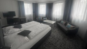 A hotel room with a large bed, a sofa, a small table, and a TV. - Panorama Hotel Rheinkrone (Andernach)