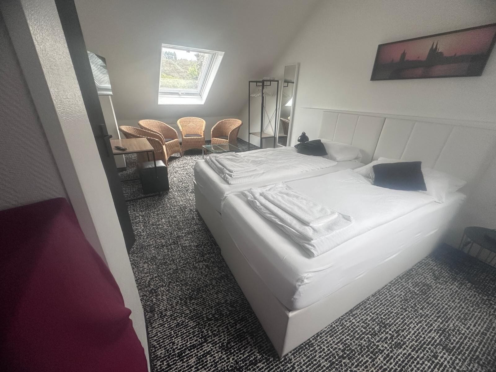 A hotel room with two beds, a large window, a chair, and a painting on the wall.