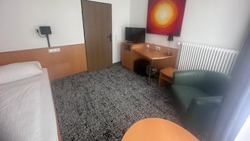 Habitación de hotel con cama, escritorio, silla, televisor y un cuadro en la pared.