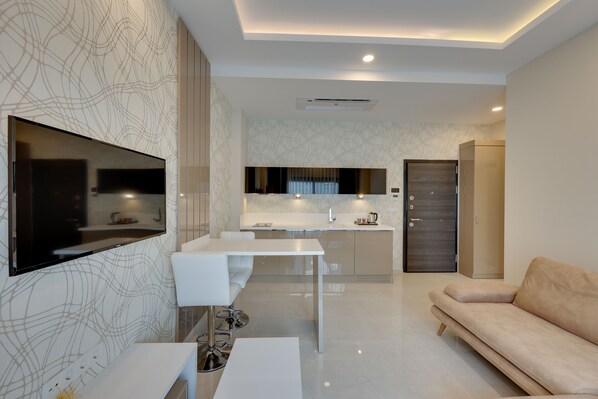 Een moderne woonkamer met een flatscreen-televisie, een witte bank, een eettafel en een keuken in de achtergrond.