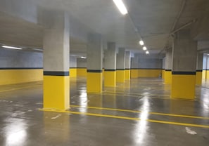 Een parkeergarage binnen, met gele en grijze pilaren, betonvloeren en verlichting aan het plafond.