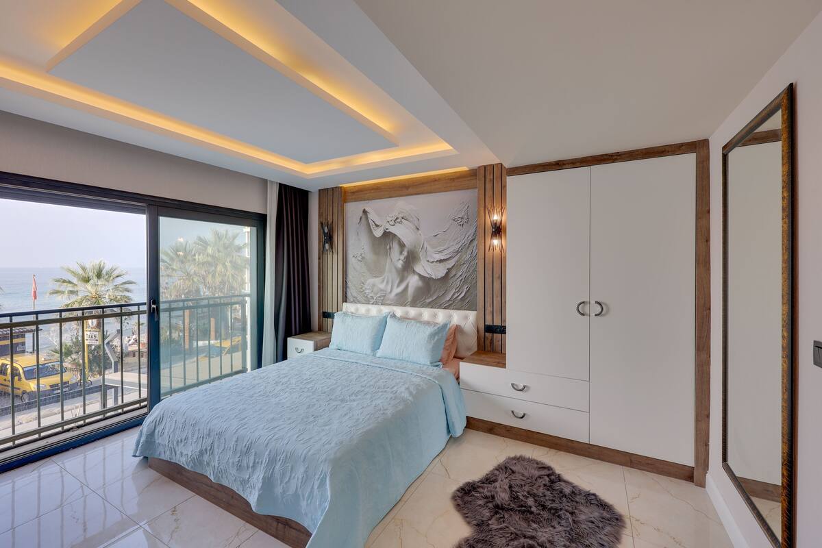 Une chambre dotée d’un grand lit, d’une armoire, d’une table de chevet, d’une vue sur la mer et d’un balcon.