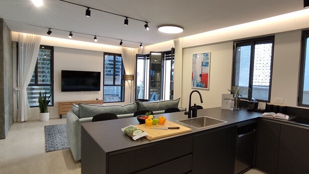 A modern kitchen with a central island, a dining area with a sofa, and a large window providing natural light. - JAFFA - Authentic Collection - By HOMY (Tel Aviv)