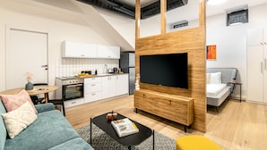 A modern living room with a flat-screen TV, a sofa, a coffee table, and a kitchen in the background. - JAFFA - Authentic Collection - By HOMY (Tel Aviv)