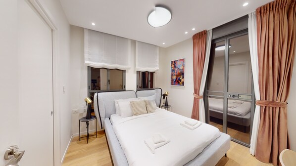 A modern bedroom with a large bed, a bedside table, a lamp, and a sliding glass door to a balcony.