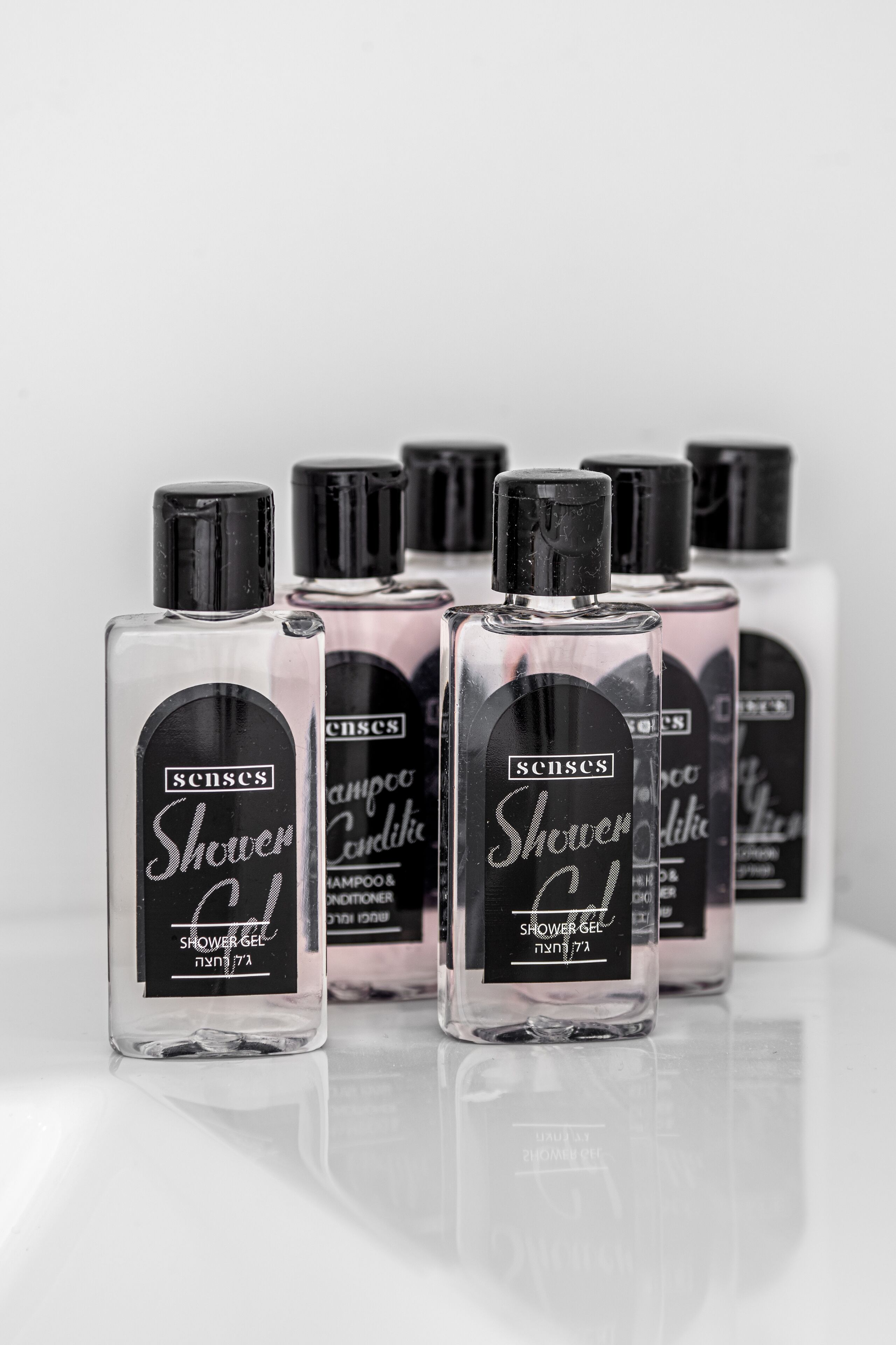 Una hilera de botellas de vidrio transparente con tapones negros, cada una etiquetada como 'Senses Shower Gel'.
