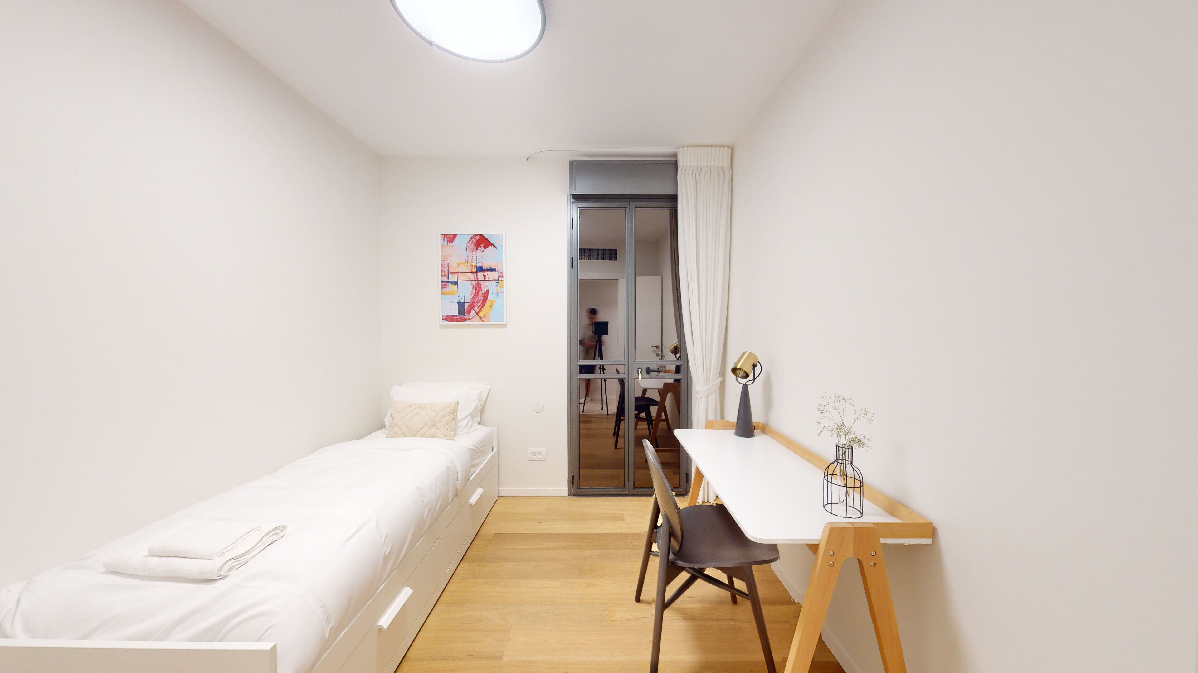 Ein kleines, ordentlich eingerichtetes Schlafzimmer mit einem Einzelbett, einem Schreibtisch und einem Stuhl.