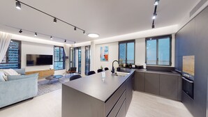 A modern kitchen with a central island, a dining area with a round table, and a living room with a sofa and TV. - JAFFA - Authentic Collection - By HOMY (Tel Aviv)