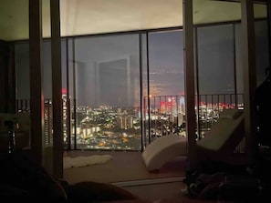 Une chambre située dans un immeuble de grande hauteur, avec une grande fenêtre donnant sur une vue panoramique de la ville la nuit.