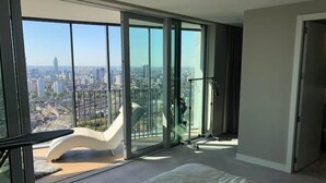 A modern bedroom with a large bed, a white chair, and a city view through floor-to-ceiling glass windows. - Stunning city penthouse with 360-degree skyline views (London)