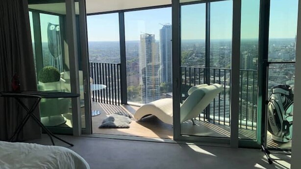 A modern hotel room with a large sliding glass door leading to a balcony with a city view. - Stunning city penthouse with 360-degree skyline views (London)