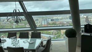 A modern office space with a large glass window offering a city view. - Stunning city penthouse with 360-degree skyline views (London)