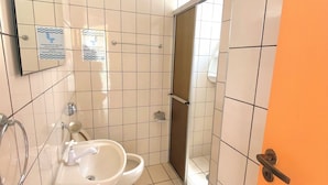 Un baño con lavabo, inodoro y zona de ducha. Hay letreros en la pared y una puerta a la derecha.