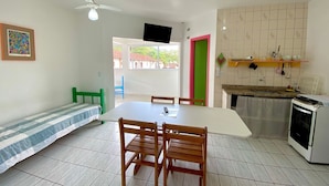 Un comedor con una mesa y sillas, un ventilador de techo, un televisor montado en la pared y una cocina con estufa y fregadero.