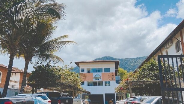 Un estacionamiento con coches, un edificio con un letrero, palmeras y una montaña al fondo.