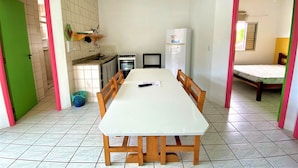 Cocina compacta con comedor, refrigerador y una cama en la habitación contigua.