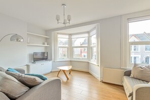 En moderne stue med sofa, sofabord, fjernsyn og et karnapvindue med udsigt til bygninger.