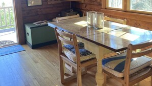 L’intérieur d’un chalet en bois comprend une table à manger, des chaises, un téléviseur et une fenêtre donnant sur la forêt.