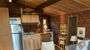 L’intérieur chaleureux d’un chalet avec un plancher en bois, une table à manger, un canapé, un fauteuil et un coin cuisine équipé d’un réfrigérateur, d’une cuisinière et de placards.