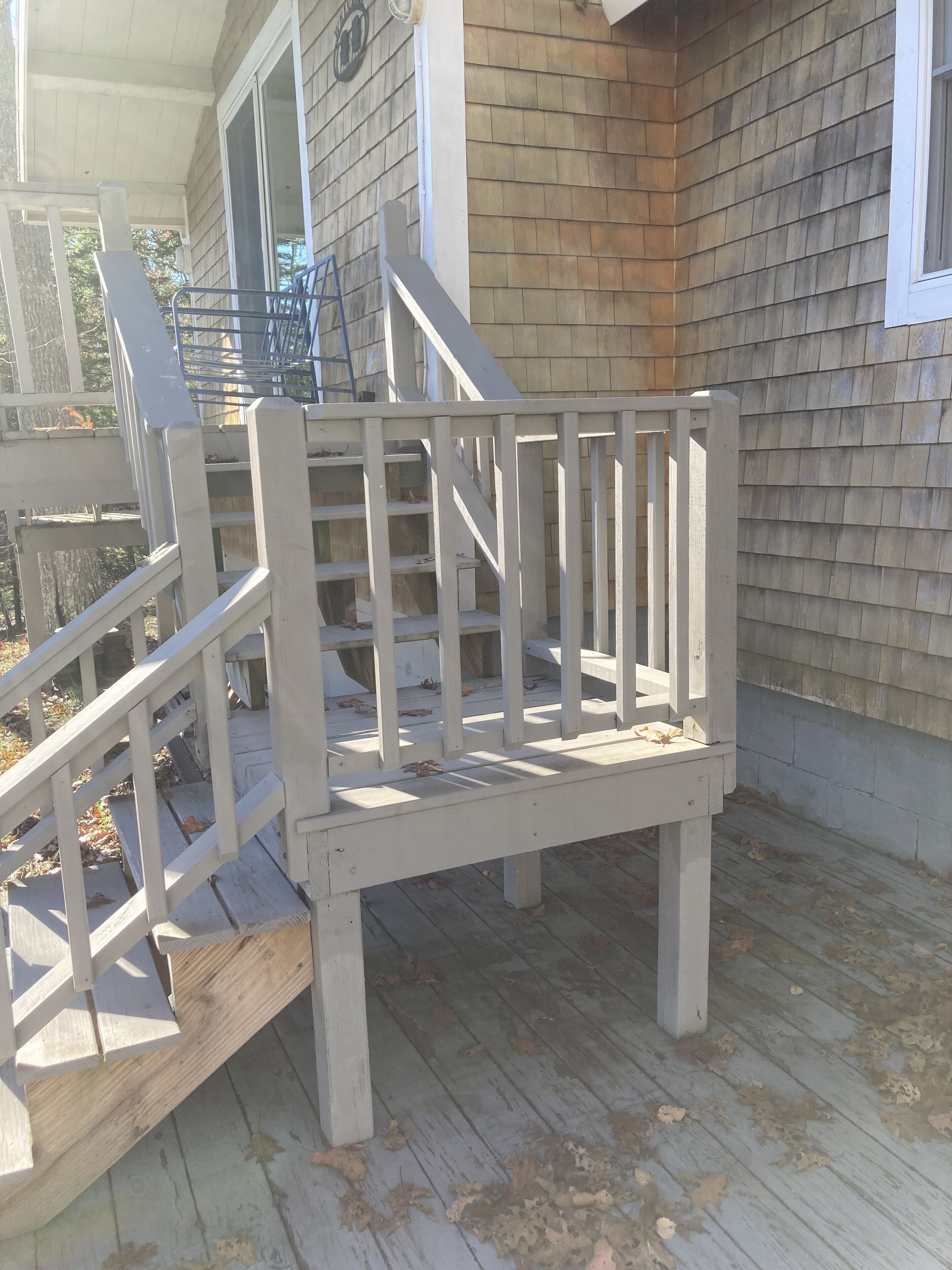 Une terrasse en bois avec une balustrade blanche et des marches menant à une maison.