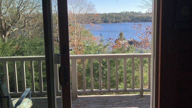 Une vue depuis une porte-fenêtre coulissante donnant sur une terrasse avec un banc et un paillasson, avec en arrière-plan un lac et des arbres.