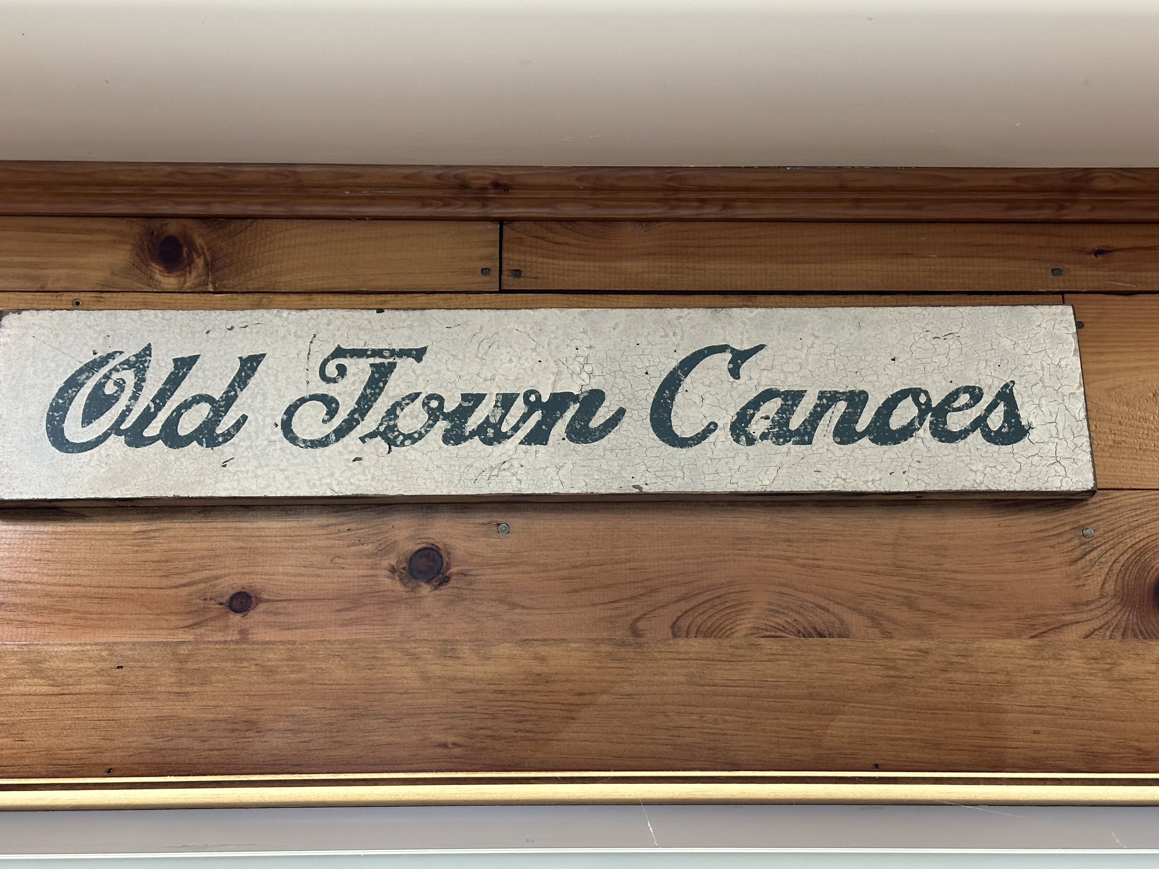 Une enseigne en bois portant l’inscription « Old Town Canoes » est fixée à un mur.