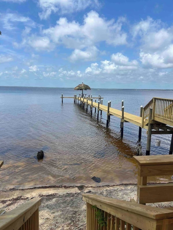 A wooden pier extending into calm waters with a thatched umbrella at the end. - Tubbies on the Bay (Pensacola)