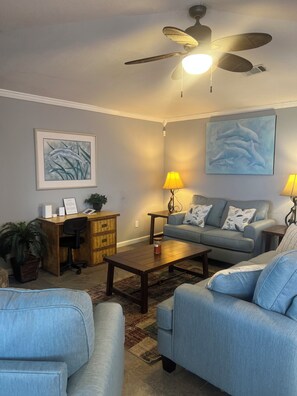 A living room with a ceiling fan, a sofa, a coffee table, and a desk with a lamp. - Secluded Waterfront Home on the Bay (Pensacola)