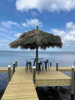 A wooden dock with a thatched umbrella and four chairs. - Tubbies on the Bay (Pensacola)