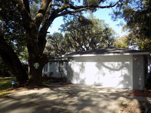 A residential garage with a white exterior, surrounded by mature trees and a clear sky.