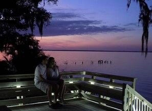 Una pareja sentada en un muelle de madera con vista a una masa de agua tranquila al anochecer.