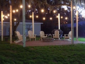 An outdoor seating area with chairs and tables, string lights overhead, and a building in the background. - Tubbies on the Bay (Pensacola)