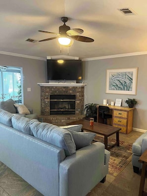 A living room with a sofa, fireplace, TV, ceiling fan, and a framed picture on the wall. - Tubbies on the Bay (Pensacola)