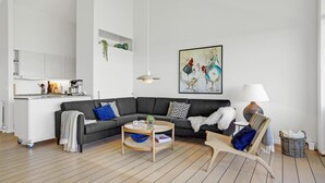 En moderne stue med en grå hjørnesofa, et sofabord, en fletstol, en lampe og et billede på væggen.