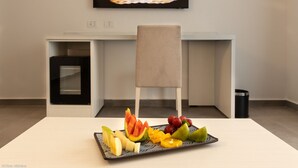 Un comedor moderno con una mesa blanca, un plato de fruta, una silla y un televisor mostrando comida.
